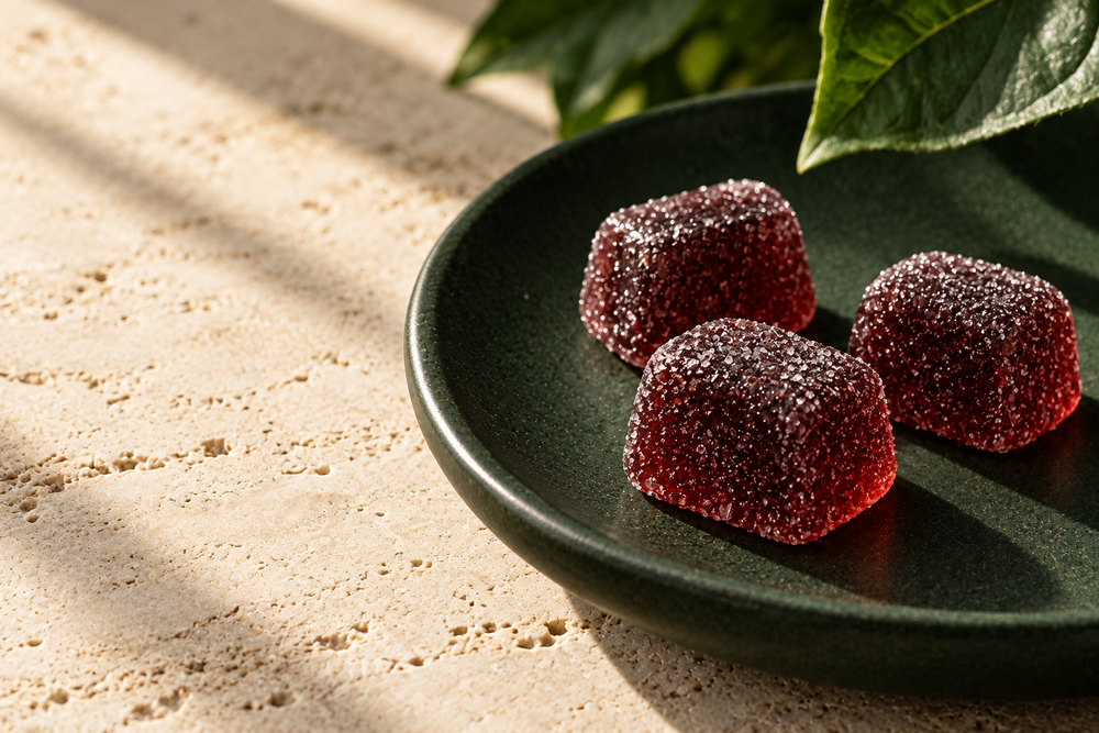 Close-up illustration of three sugar-dusted cherry-red gummies on a forest-green ceramic dish