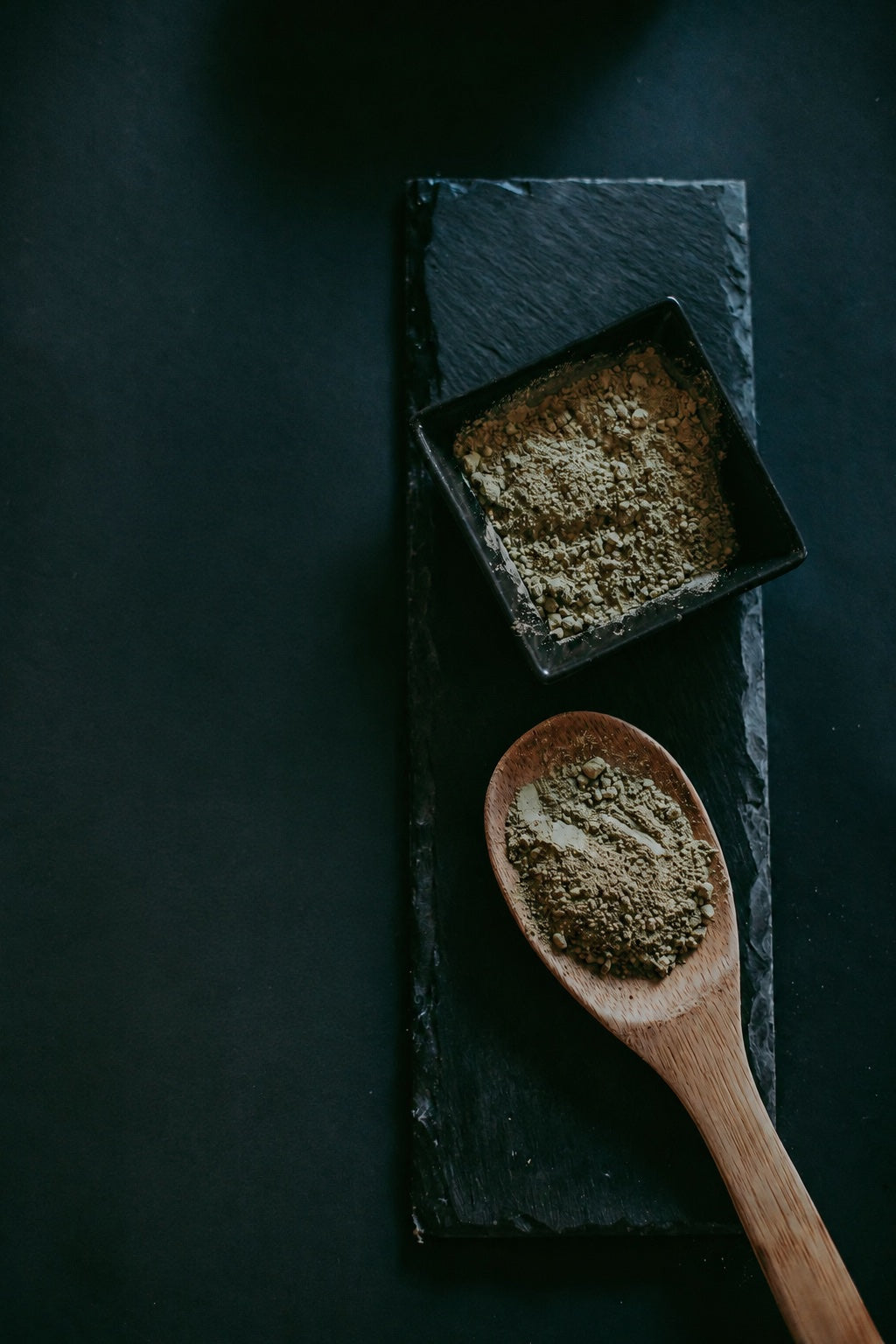 Kratom powder in a black bowl and on a wooden spoon